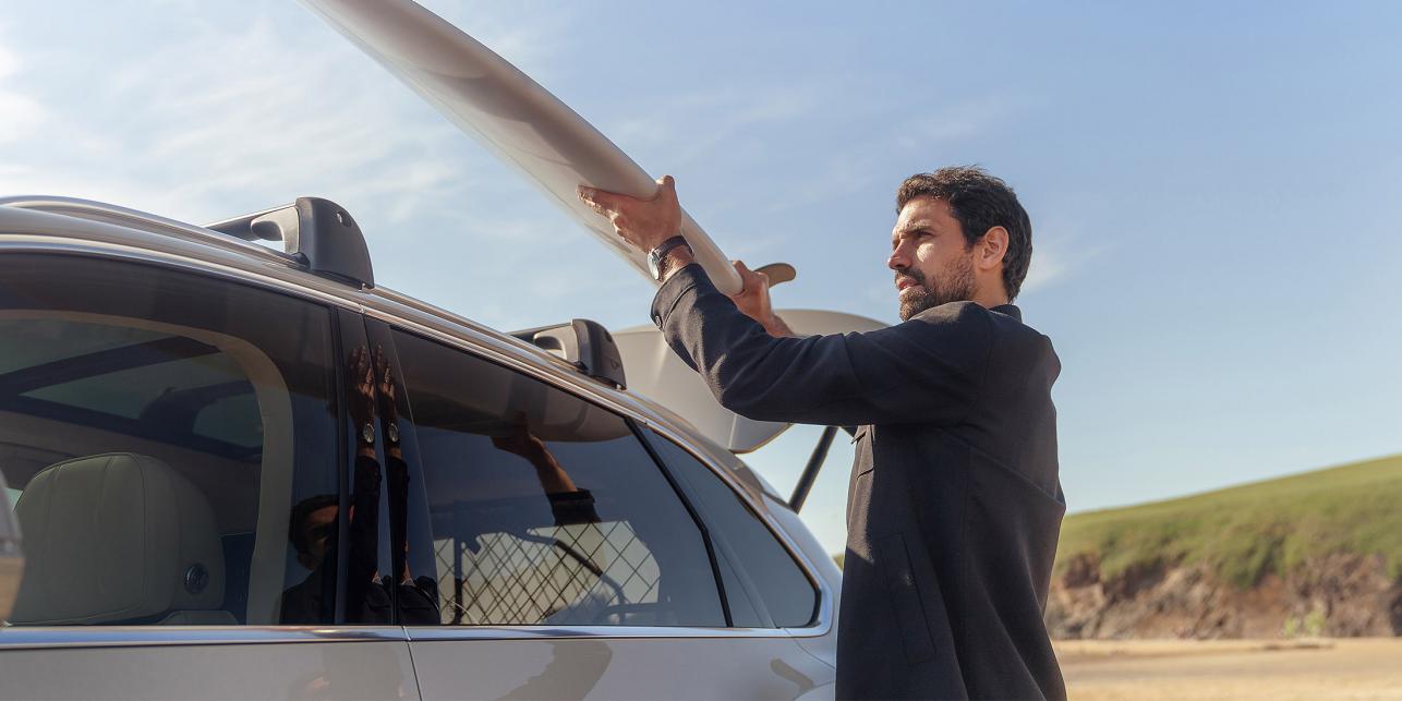 Surfer removing his surf board from the roof of a Bentayga benefitting from fixed roof bars