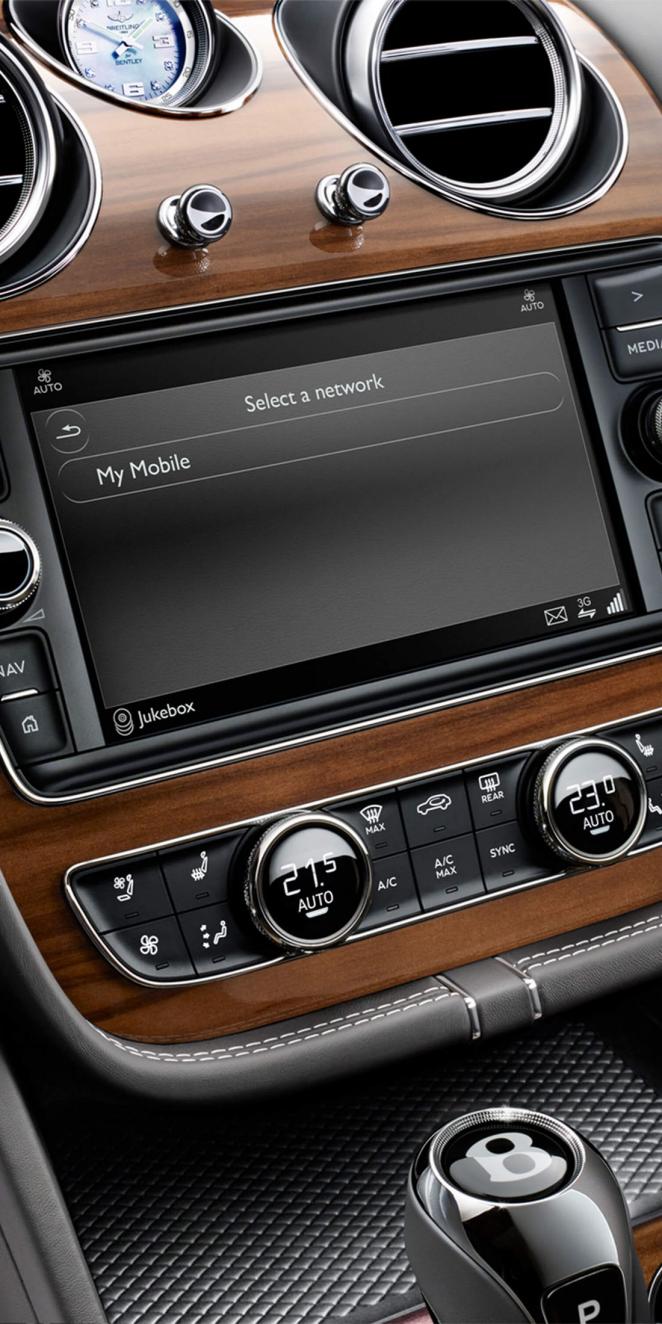 Close up view of Bentley Bentayga's 10.1 inch infotainment screen, set in Open Pore Crown Cut Walnut veneer, with hard buttons at bottom