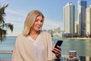 A person/lady/individual looking at Smartphone, with high rise buildings in backdrop.