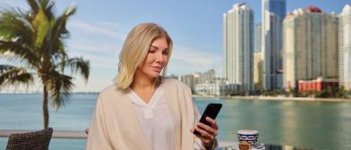 A person/lady/individual looking at Smartphone, with high rise buildings in backdrop.