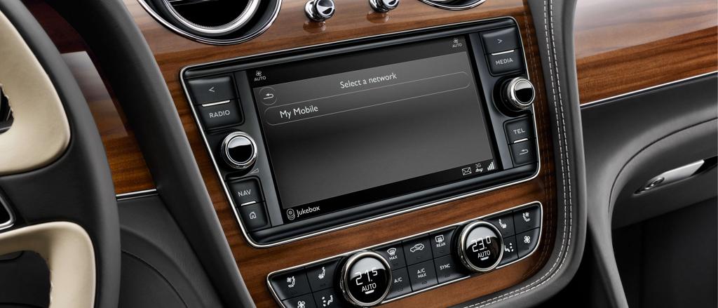 Close up view of Bentley Bentayga's 10.1 inch infotainment screen, set in Open Pore Crown Cut Walnut veneer, with hard buttons at bottom