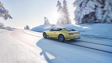 Rear side angled view of Bentley Continental GT Azure in Julep, effortlesly driving along snow covered road