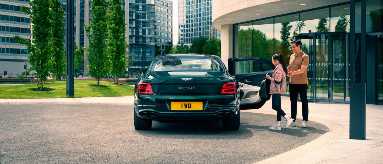 Rear view of Bentley Flying Spur in Verdant Green, with right passenger door open, parked with buildings and two people in view