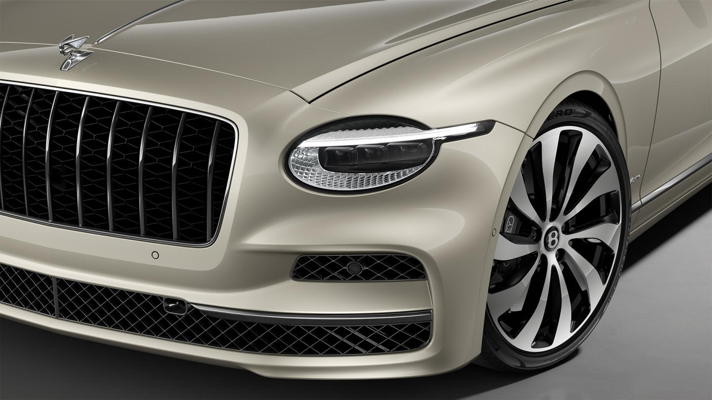 Front three-quarter close-up of the Bentley Flying Spur Azure in White Sand showing the headlights and 22" Ten Spoke Wheel painted in black and bright machined.