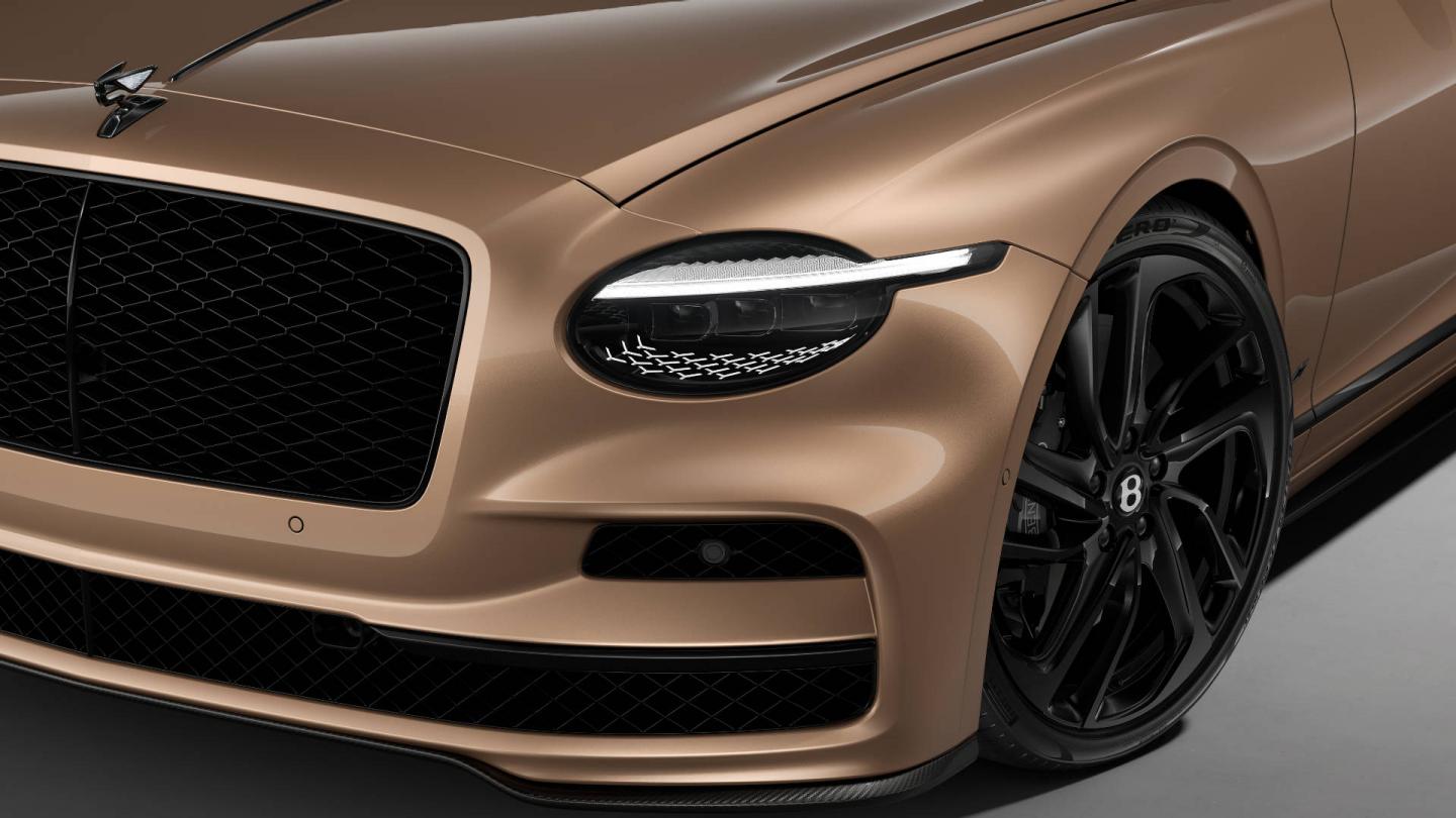 Front three-quarter close-up of the Bentley Flying Spur S in Rose Gold showing the headlights, Carbon Styling Spec and 22" Ten Swept Spoke wheel painted in black.